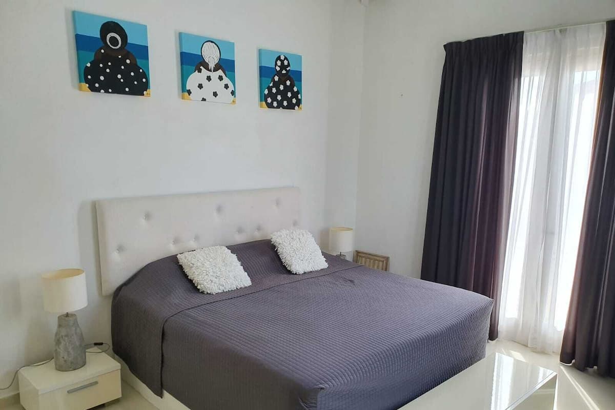 A bedroom with a bed, two bedside tables, a lamp, and three wall-mounted artworks.