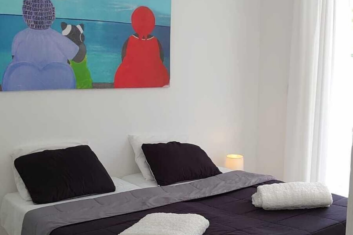 A bedroom with a bed, pillows, a blanket, and a painting on the wall.