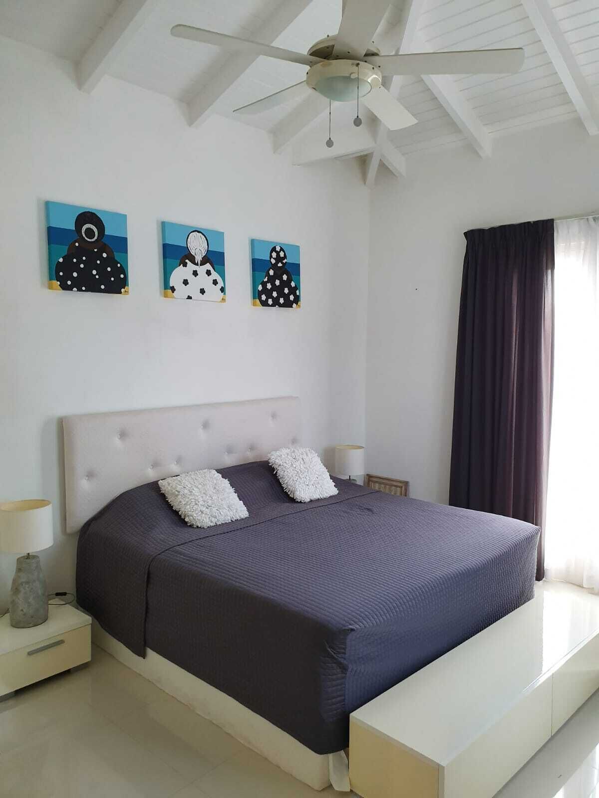 Een slaapkamer met een groot bed, een plafondventilator en drie wanddecoraties.