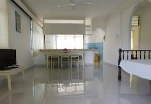 A spacious room with a dining area, a TV on a stand, and a balcony with a railing.