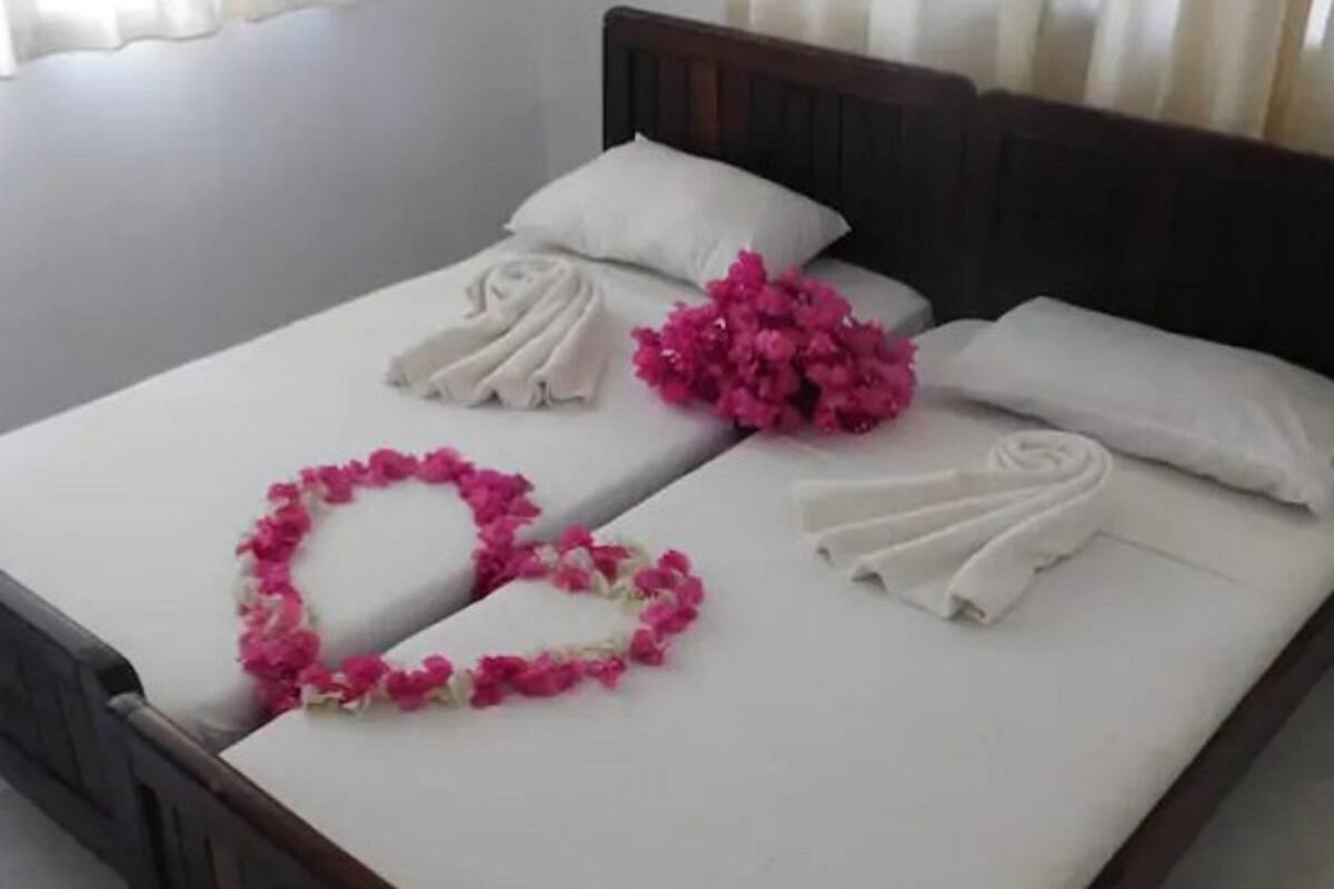 Cama bem arrumada com lençóis brancos, guirlandas de flores cor-de-rosa e toalha enrolada.