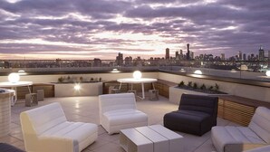 A rooftop terrace with modern seating, a city skyline view, and a sunset sky. - YARRA · YARRA Toorak Rd & Chapel St. Pool, Gym & Parking (South Yarra)