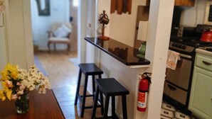 A kitchen with a wooden table, stools, hanging pots, a fire extinguisher, and a patterned floor.