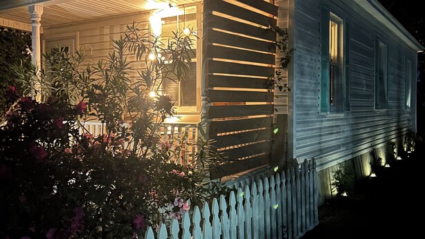 A house with a porch, a white picket fence, and a garden with pink flowers.