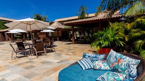 Un patio con mobiliario de mimbre, un sofá redondo con cojines estampados y sombrillas que dan sombra.