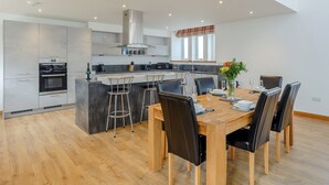 A modern kitchen with a central island, bar stools, and a dining table set for six. - 3 bedroom accommodation in Woodhead, near Turriff (Woodhead, near Turriff)