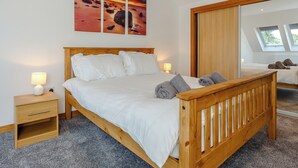 A bedroom with a wooden bed, white bedding, a nightstand, a lamp, and a large mirror. - 3 bedroom accommodation in Woodhead, near Turriff (Woodhead, near Turriff)