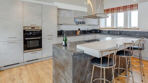 A modern kitchen with a central island, stainless steel appliances, and a bar area with stools. - 3 bedroom accommodation in Woodhead, near Turriff (Woodhead, near Turriff)