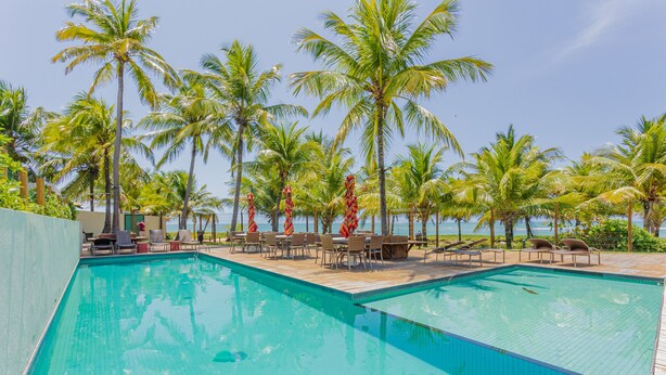 A swimming pool with lounge chairs and tables, surrounded by palm trees and a clear sky.