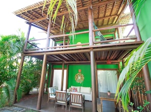 A two-story wooden structure with a balcony, surrounded by lush greenery.