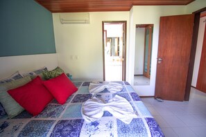 A bedroom with a bed, pillows, a wooden door, and a hallway.