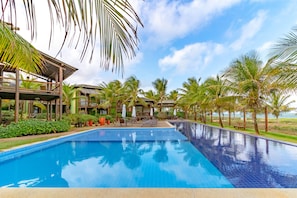A swimming pool with lounge chairs and umbrellas, surrounded by palm trees and a wooden building. - IT70 Ótimo bangalô duplex à beira-mar (Camaçari)