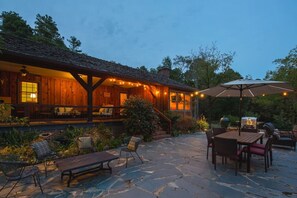 Ein rustikales Holzgebäude mit überdachter Terrasse, Steinboden, Gartenmöbeln und Lichterketten.
