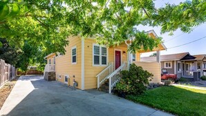 A yellow single-story house with a red door, a front porch, and a small front yard. - @ Marbella Lane - MiniGuest House | DTWN SJ | Parking (San Jose)
