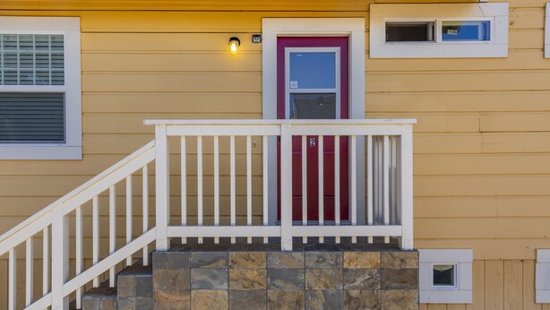 Una casa amarilla con puerta roja, barandillas blancas y una escalera de piedra.