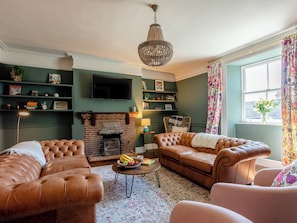 A living room with a fireplace, leather sofas, a television, and a chandelier.