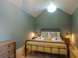 A bedroom with a bed, bedside tables, a wooden dresser, and a ceiling light.
