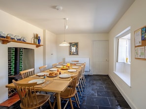 A dining area with a long table set for multiple people, chairs, a hanging light fixture, a radiator, and a window with a view.