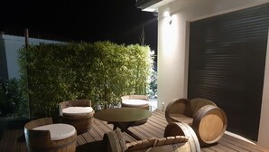 A wooden deck with round seating made from barrels, a small table, and a backdrop of green foliage. - Magnificent villa with private pool (Mirepeisset)