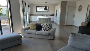 A modern living room with a grey sofa, a matching ottoman, and a kitchen in the background. - Magnificent villa with private pool (Mirepeisset)