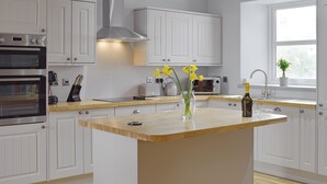 A modern kitchen with white cabinetry, a central island, a built-in oven, a microwave, and a window with a plant. - There’s more than an education to be had at The School House. (New Luce, near Newton Stewart)