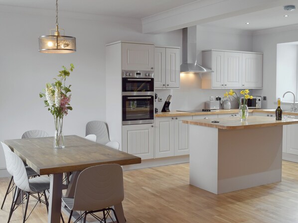 A modern kitchen with white cabinetry, a wooden dining table, and a central island.
