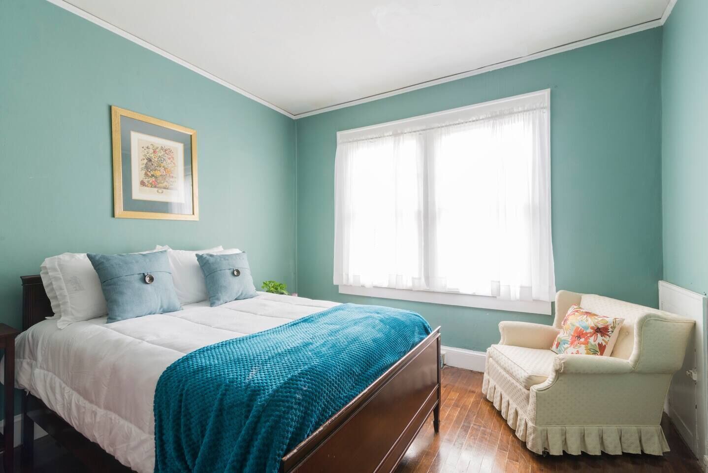 Un dormitorio con una cama, una silla, un ventanal y un cuadro en la pared.
