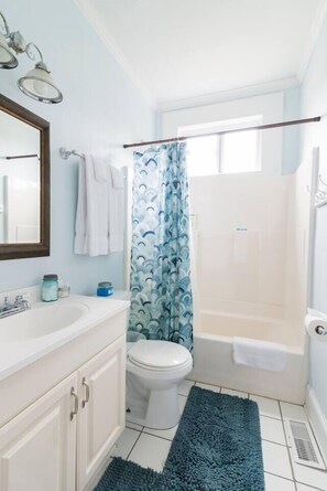 A bathroom with a white sink, mirror, and toilet, a shower with a blue curtain, and a white bathtub.