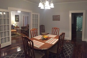 A dining room with a wooden table, chairs, and a chandelier. There is a door leading to another room and a sign on the wall that says "EAT".