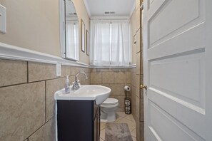 Une salle de bain avec un lavabo, des toilettes et une porte, le tout de couleur blanche.