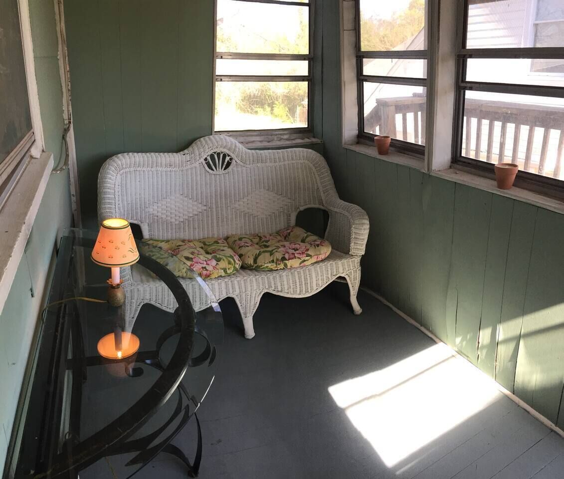 Un rincón acogedor con un sofá de mimbre, una mesita con lámpara y una ventana con vistas al exterior.