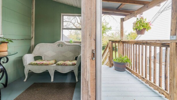 A cozy porch with a wicker sofa, a small table, and potted plants.