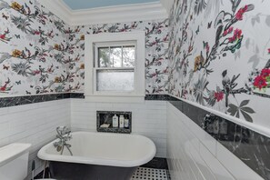 Un baño con papel tapiz floral, una bañera y una ventana.
