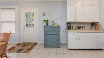 Une cuisine avec des meubles blancs, une commode bleue et une porte ornée d’un vitrail.