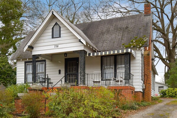 A white house with black shutters, a brick chimney, and a porch with two chairs.