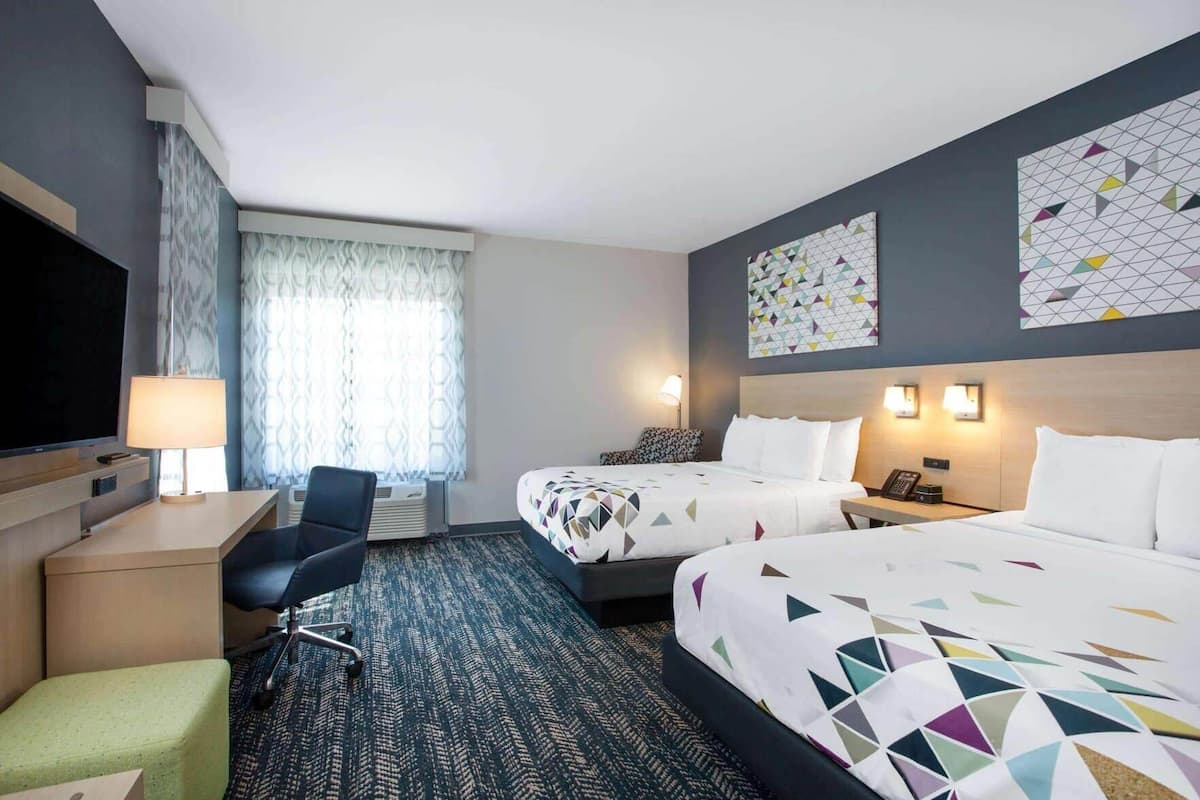 Een hotelkamer met twee bedden, een bureau, een stoel, een televisie en een raam met gordijnen.
