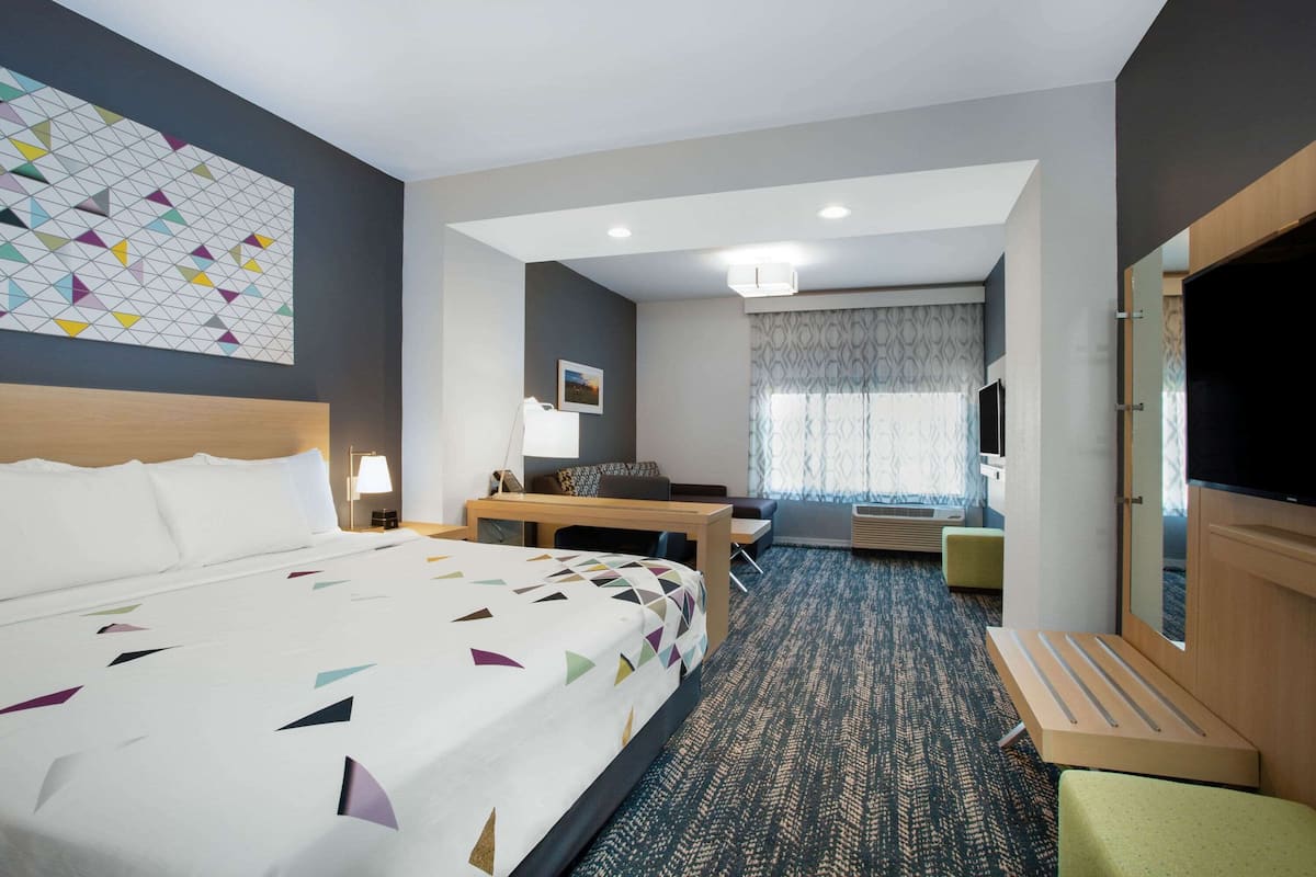 Ein Hotelzimmer mit einem großen Bett, einem Schreibtisch, einem Sessel, einem Fernseher und einem Fenster mit Vorhängen.