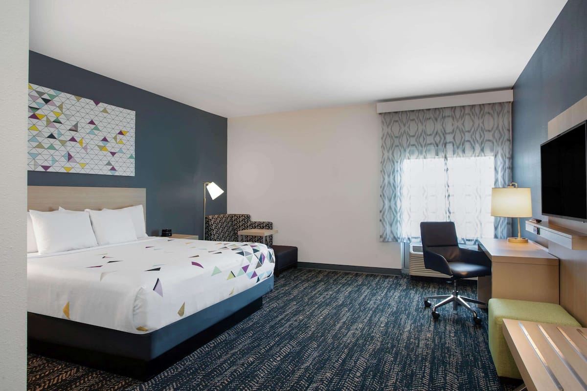 Ein Hotelzimmer mit einem großen Bett, einem Schreibtisch mit Stuhl, einem Fernseher und einem Fenster mit Vorhängen.