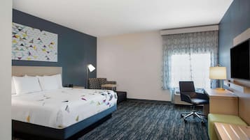 Habitación de hotel con una cama grande, un escritorio con silla, un televisor y un ventanal con cortinas.