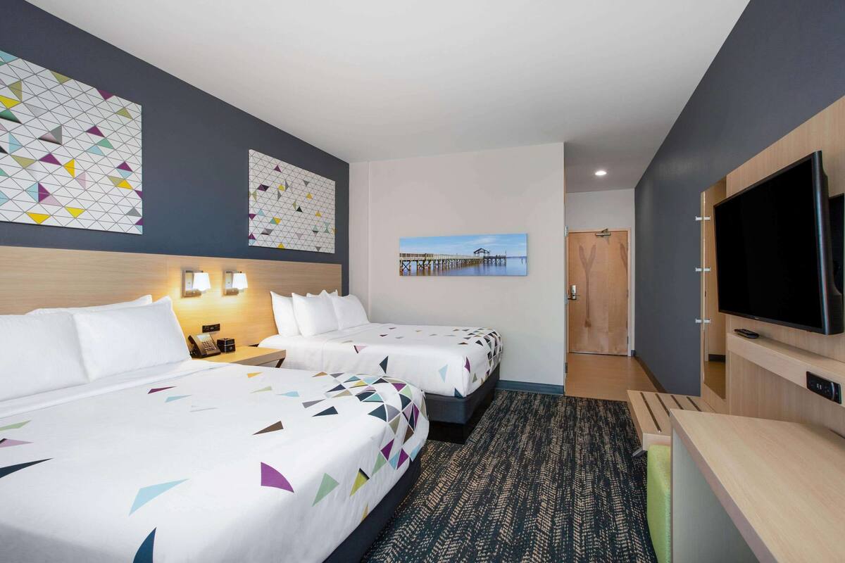 Ein Hotelzimmer mit zwei Betten, einem Fernseher, einem Schreibtisch und Bildern an den Wänden.