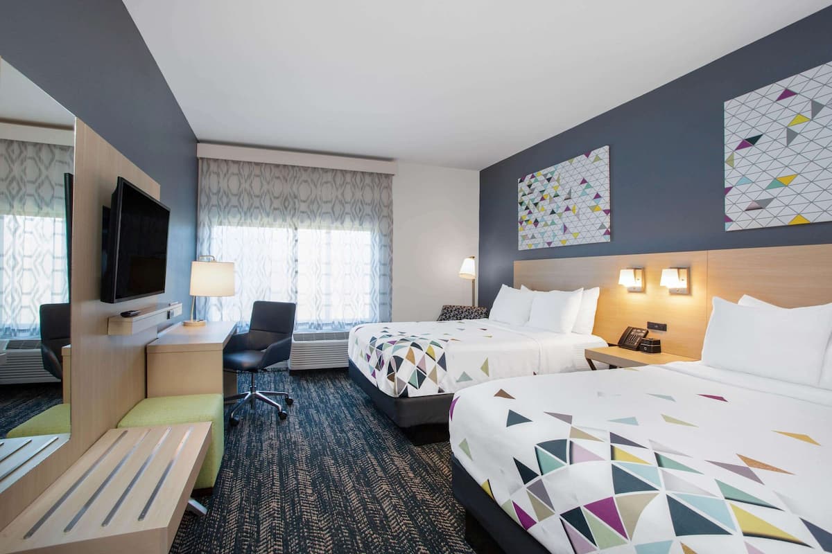 Ein Hotelzimmer mit zwei Betten, einem Schreibtisch, einem Stuhl, einem Fernseher und Bildern an den Wänden.