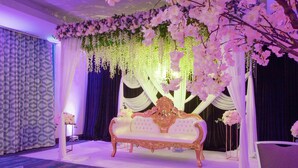 En scen med en vit soffa, blomsterdekorationer och draperade gardiner.