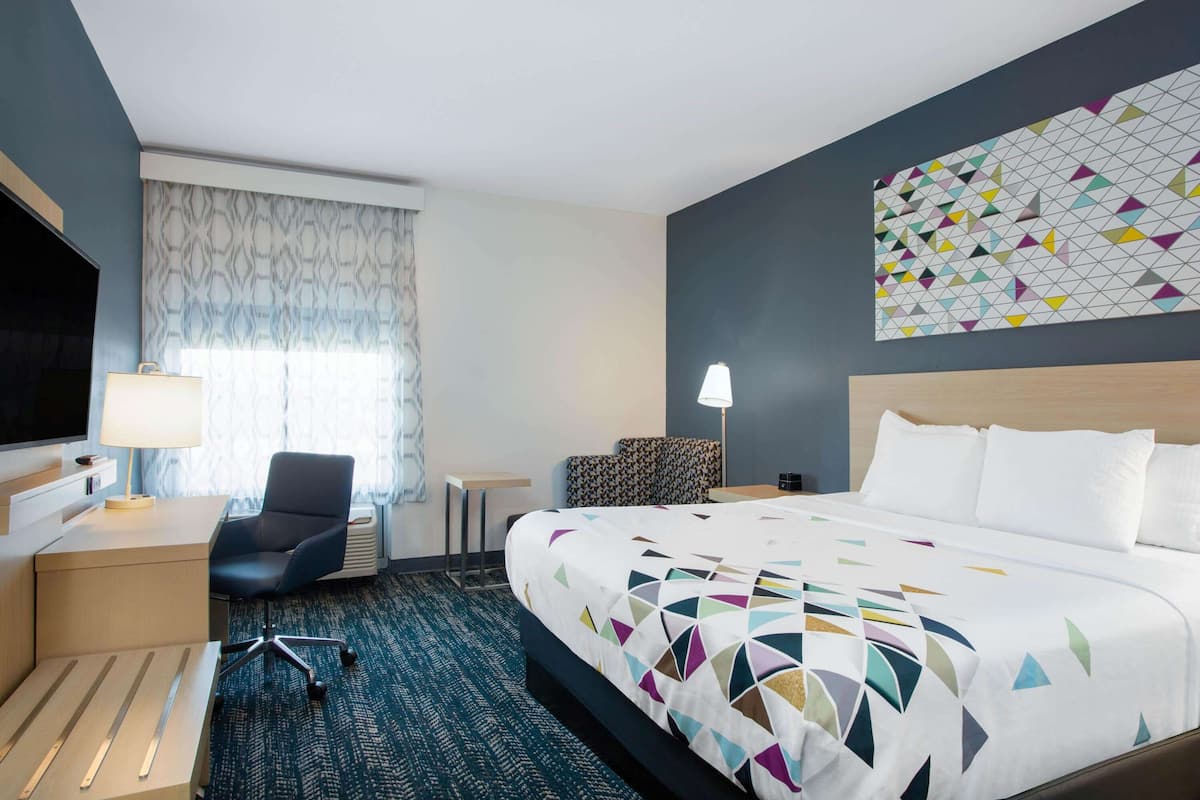 Ein Hotelzimmer mit Bett, Schreibtisch, Stuhl, Fernseher und einer Wand mit Muster.