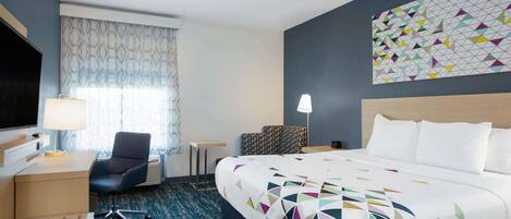 A hotel room with a bed, a desk, a chair, a TV, and a patterned wall.
