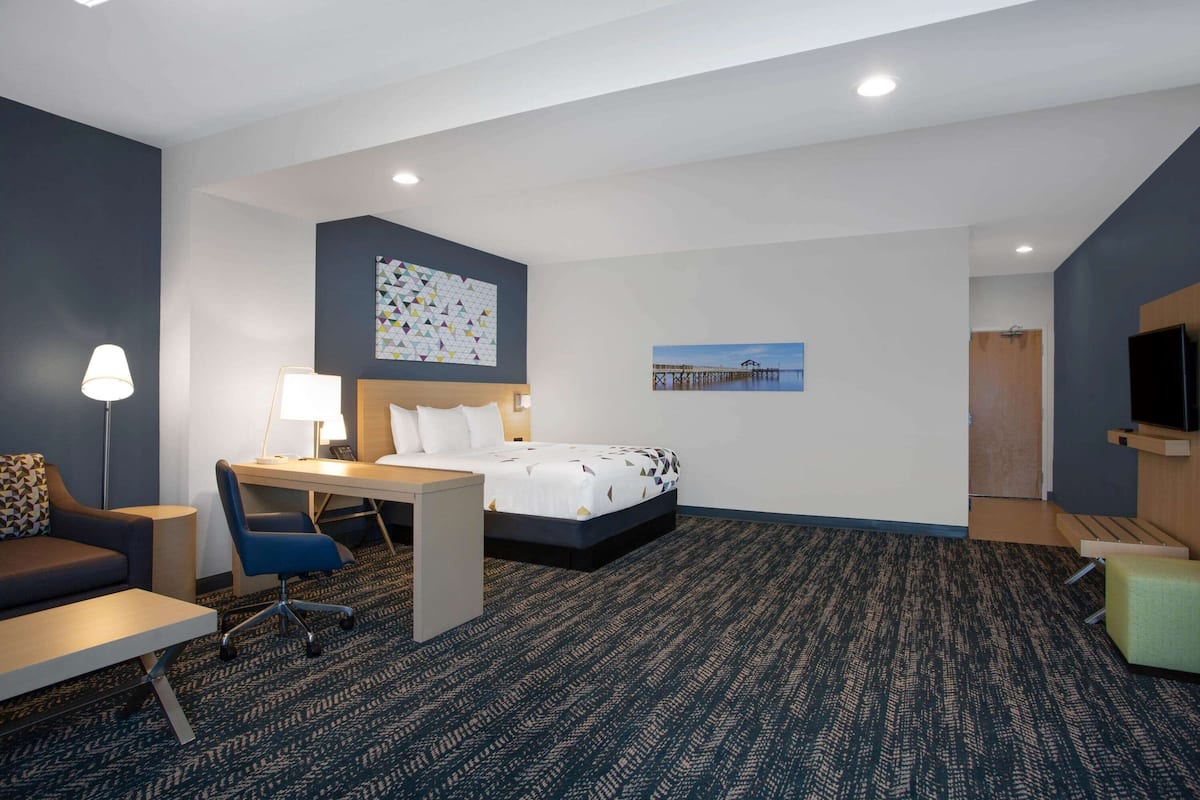 Ein Hotelzimmer mit Bett, Schreibtisch, Stuhl, Lampe und Bildern an den Wänden.