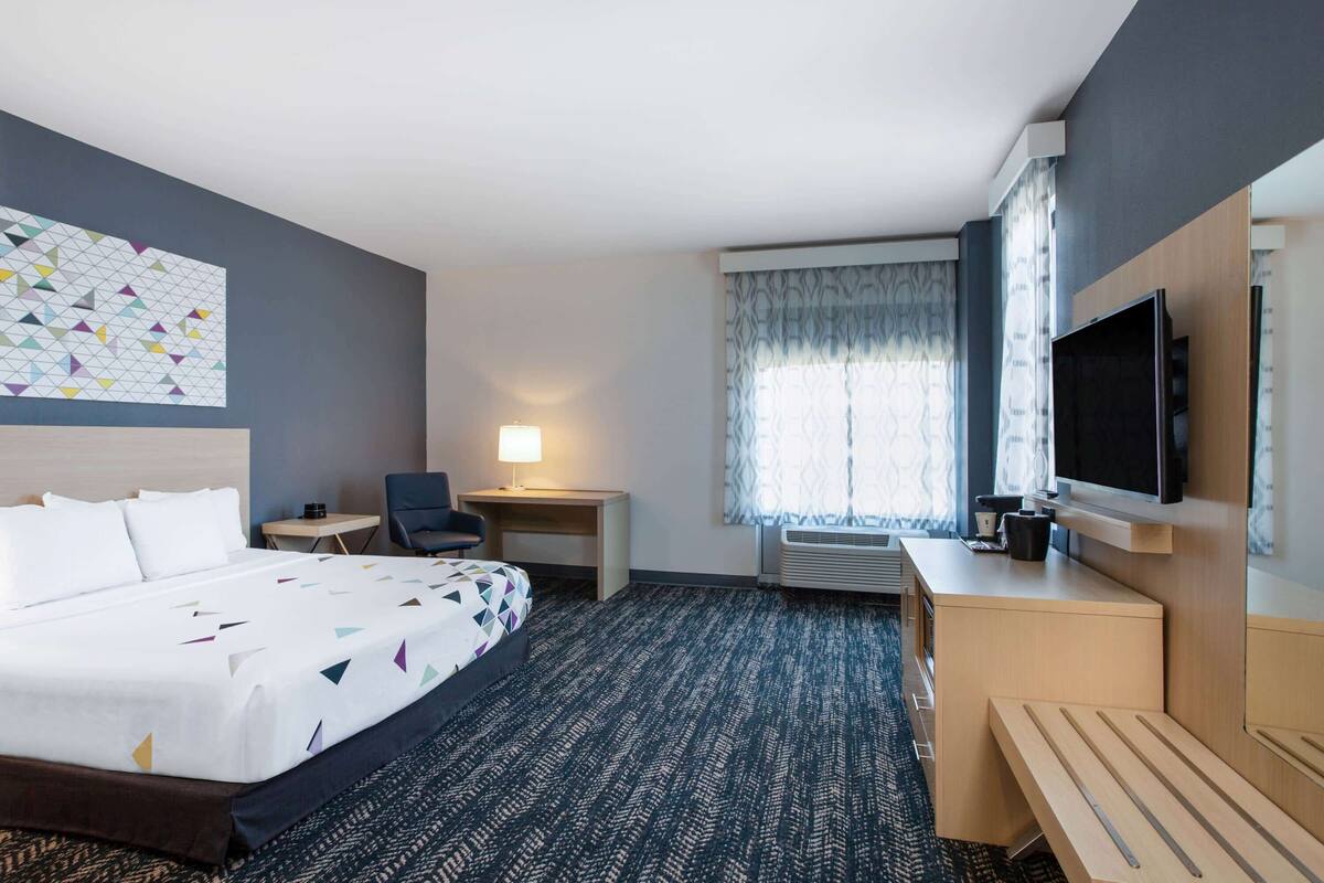 Ein Hotelzimmer mit Bett, Schreibtisch, Stuhl, Fernseher und einem Fenster mit Vorhängen.