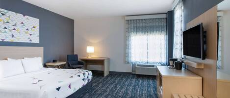 Una habitación de hotel con cama, escritorio, silla, televisor y ventana con cortinas.