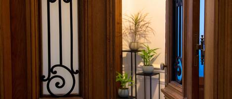 Puerta de madera con diseño de metal negro, que da a un cuarto con una planta en maceta y una mesita.