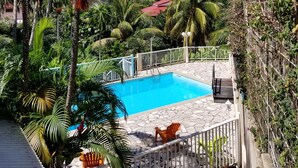 A pool area with a clear blue pool, surrounded by palm trees and a stone deck. - Studios Paradis Turquoise, swimming pool, beach, Les Trois ilets (les 3 ilets)
