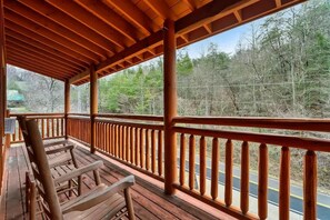 A wooden deck with a railing, benches, and a view of a forested area. - 6-Bedroom All-Ensuite Cabin with Indoor Pool & Theater Near Dollywood (Pigeon Forge)